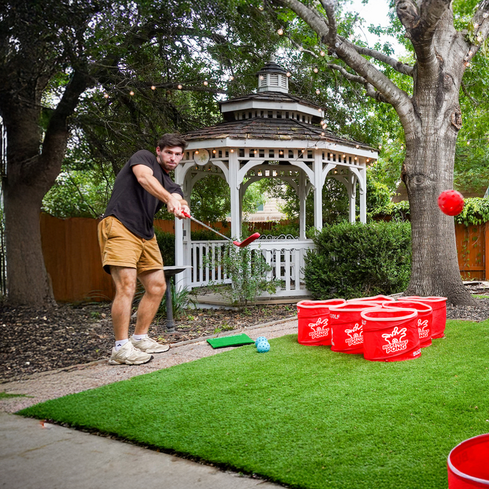 Player chipping from the turf mat toward the PopPong buckets by the gazebo